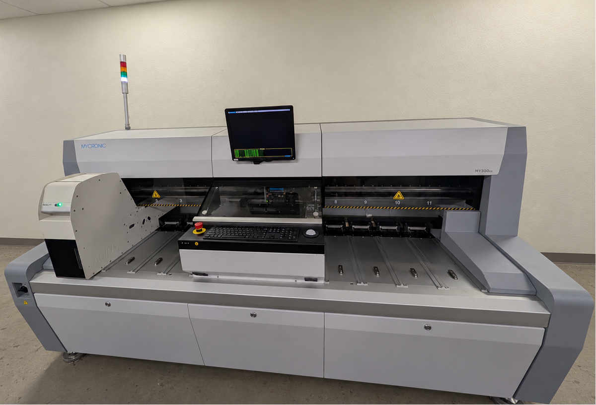 A large industrial surface-mount device (SMD) rework machine with a gray and white chassis, a built-in monitor, and a conveyor belt system, photographed in a clean utility room.